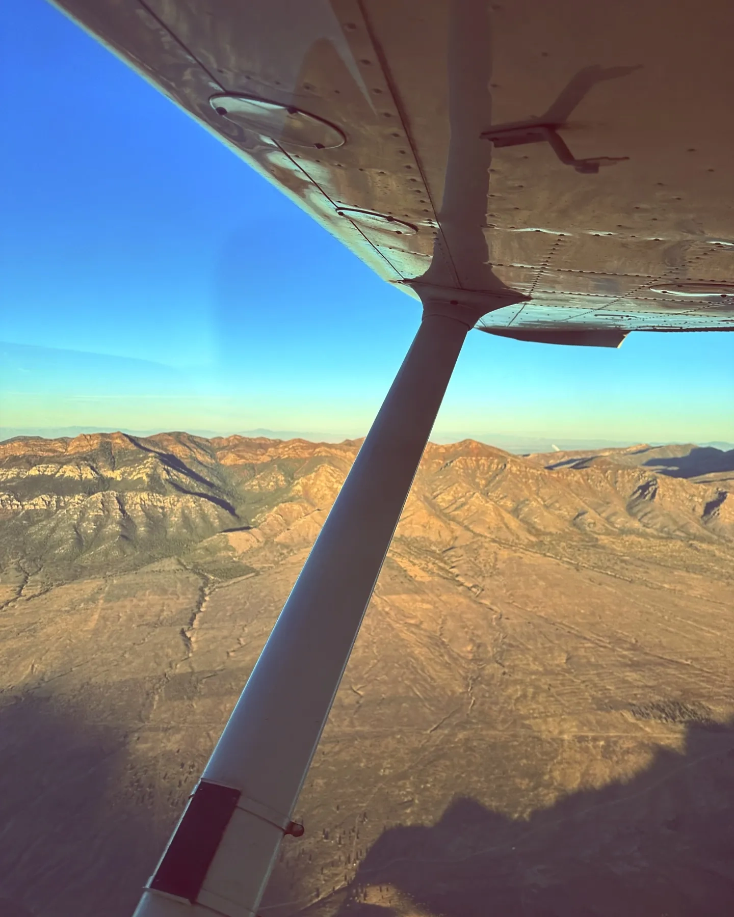 View of an airplane's wing and the ground below during flight with clear skies in the horizon
