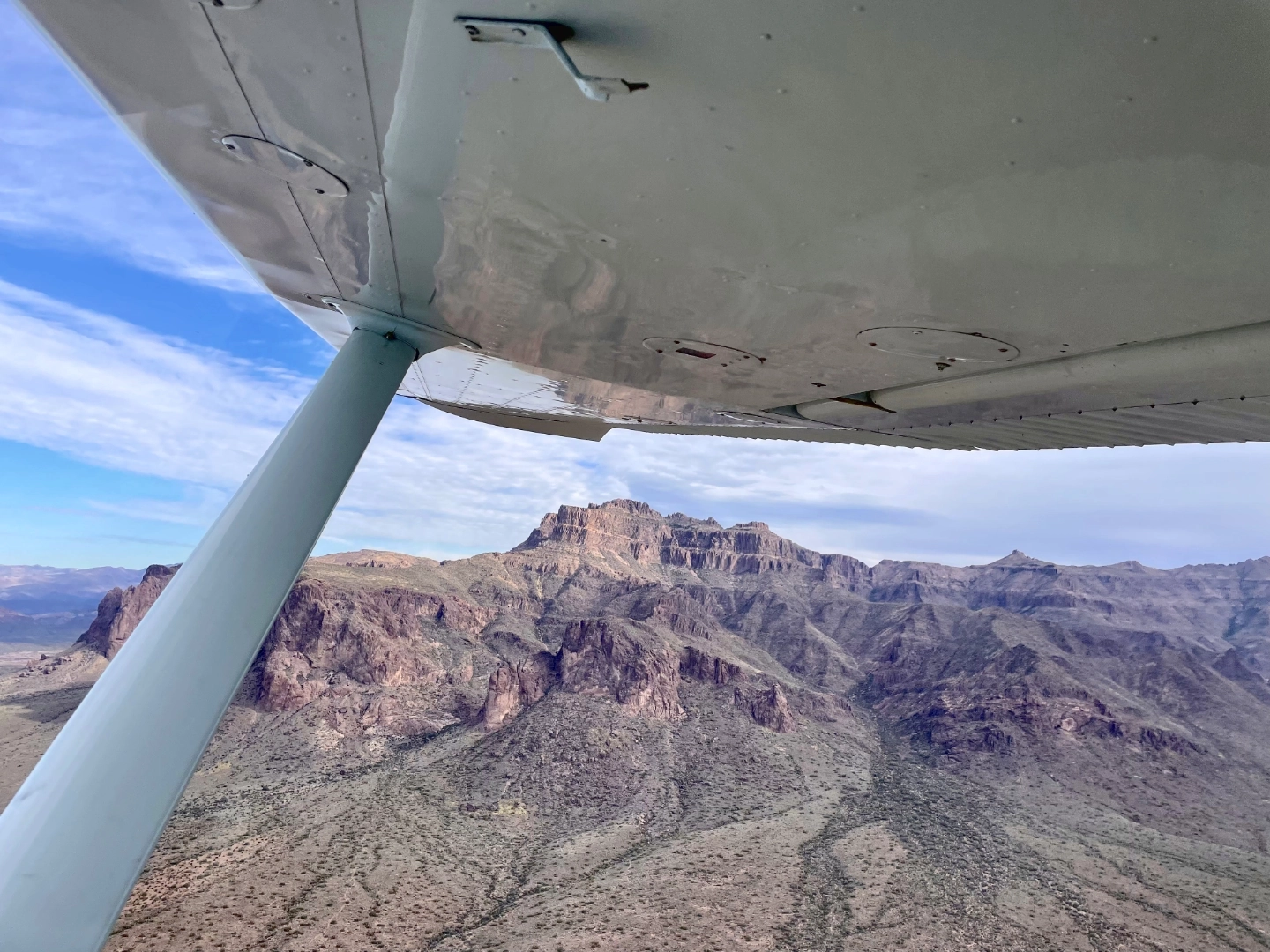 Mountains seen from a flying airplane slightly obstructed by the plane's wing