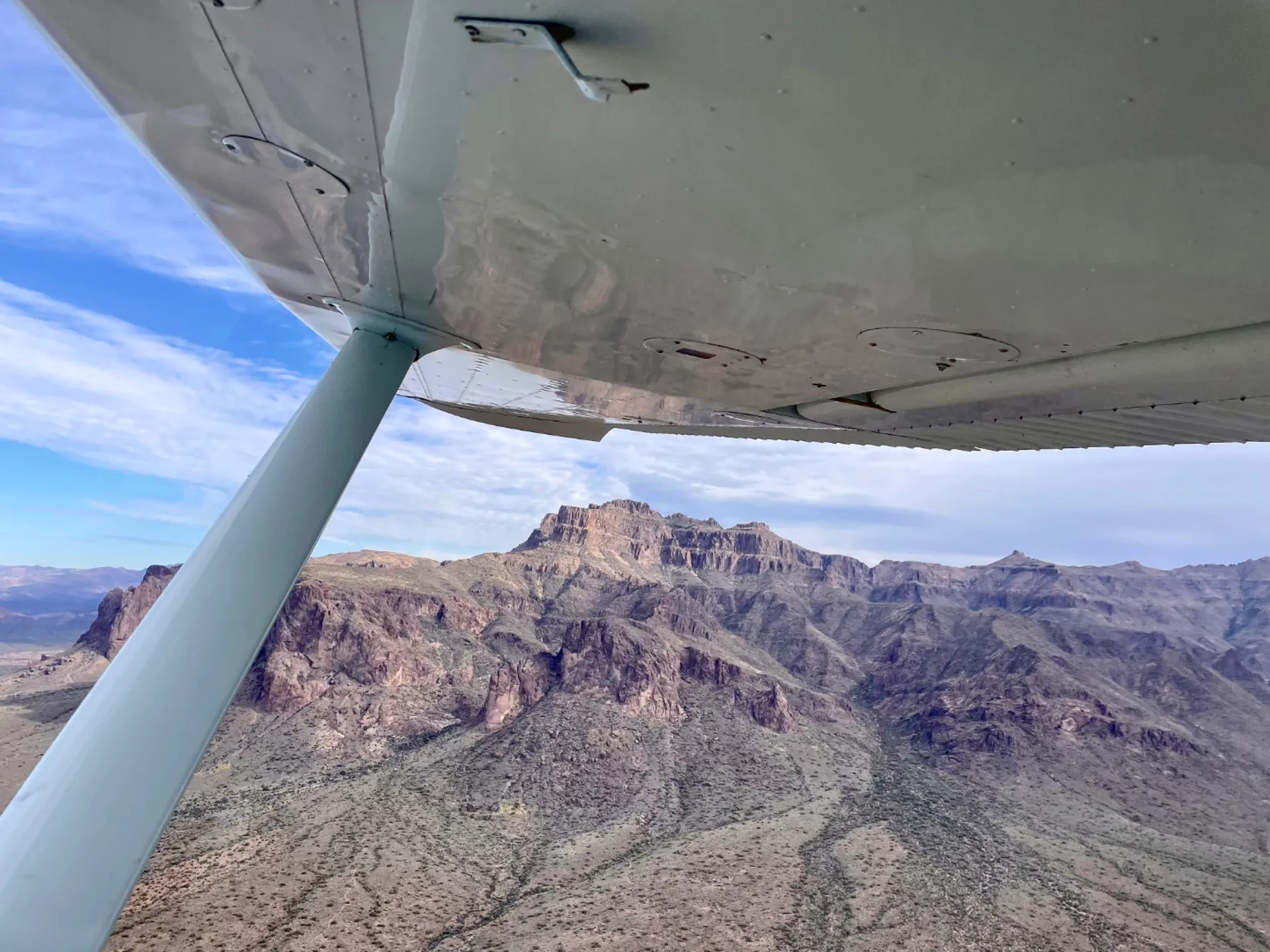 Mountains seen from a flying airplane slightly obstructed by the plane's wing