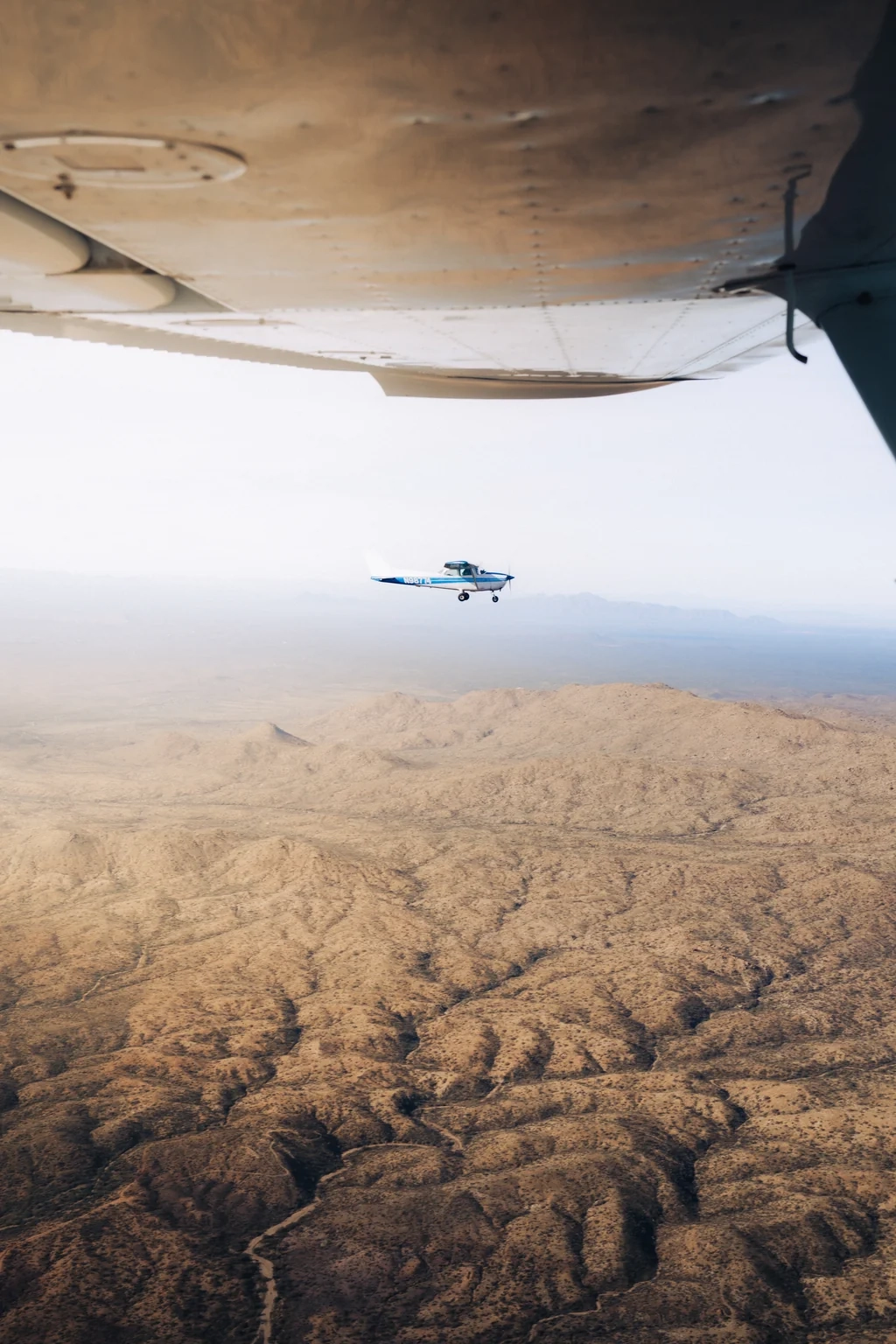 Airplane formation flying with Cessna seen from the side through the plane window with wing above and desert below