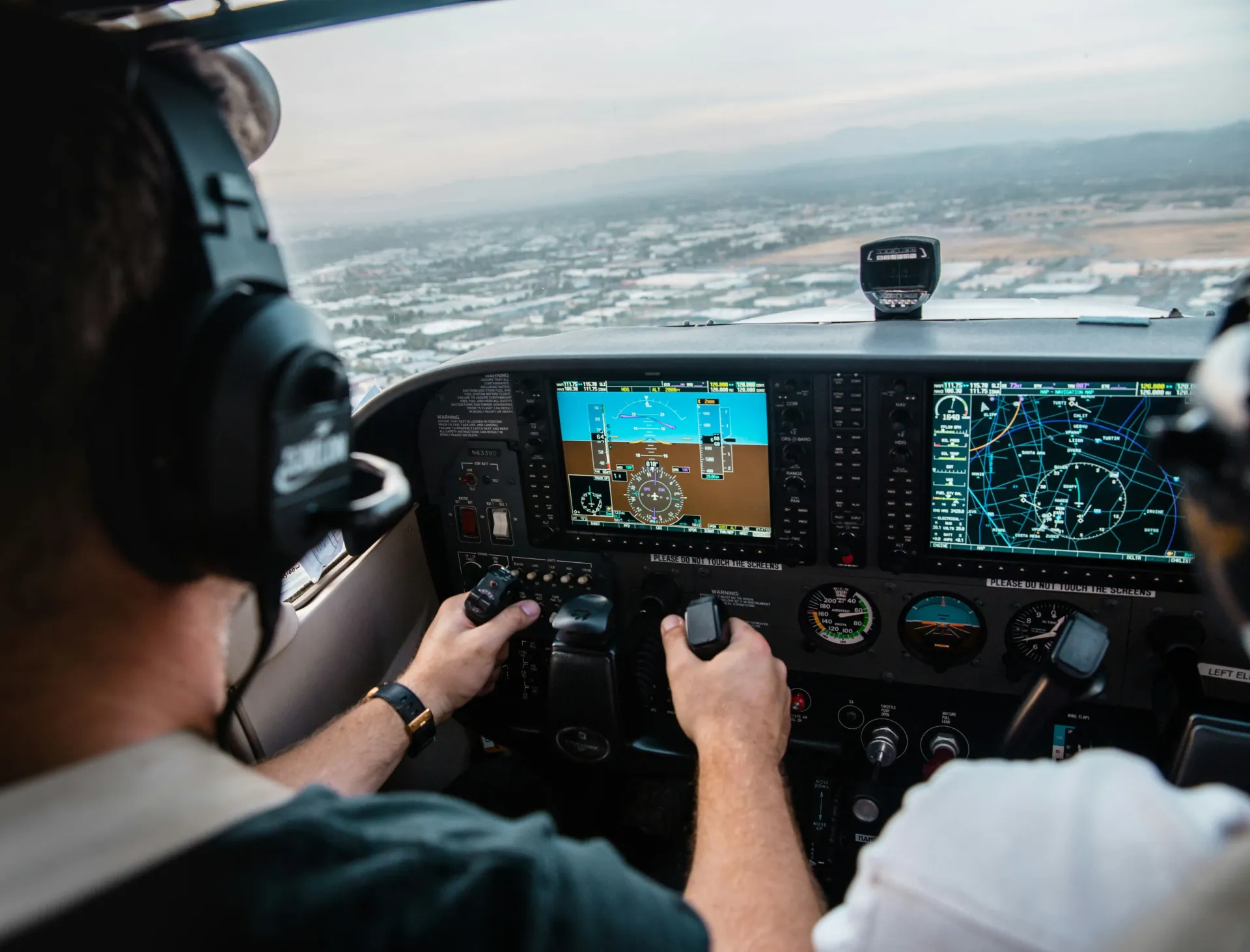 Pilot flying an airplane with an instrument panel over a cityscape