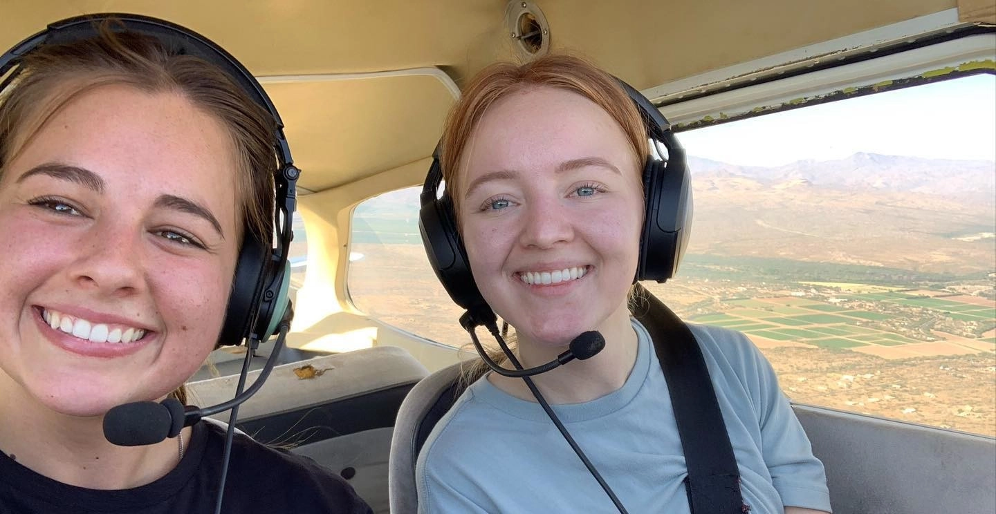 Two women pilots smiling to the camera inside flying aircraft