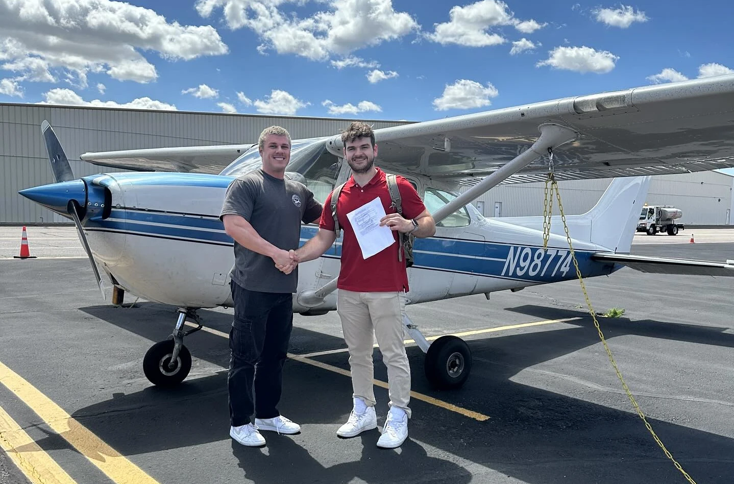 Two men shaking hands and holding a certificate in front of a Cessna 172 airplane