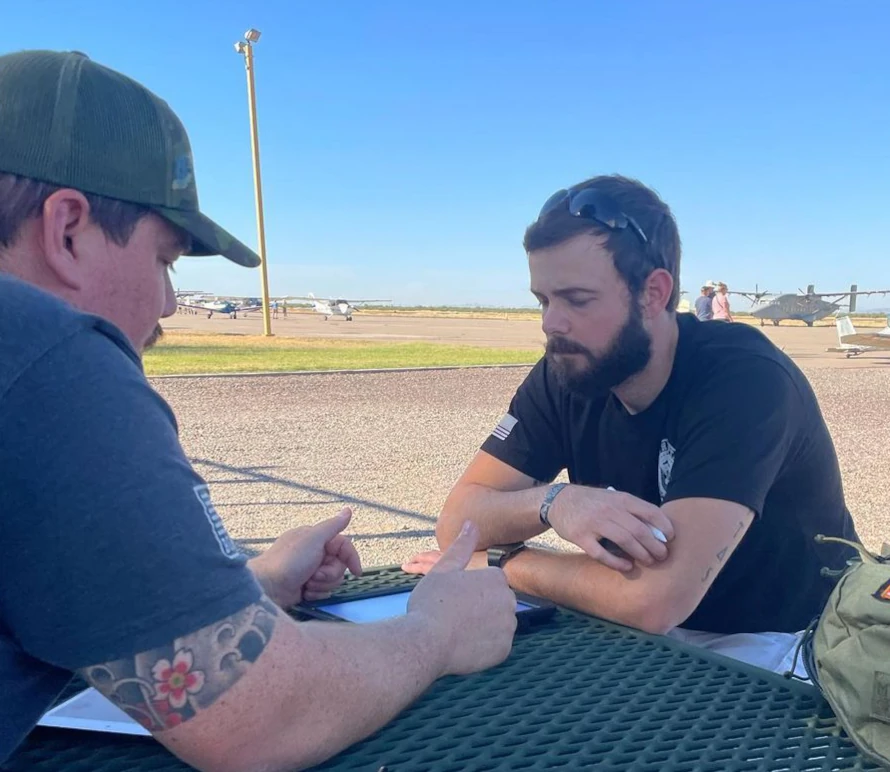 Man making explanation to another man over a table outside an airport