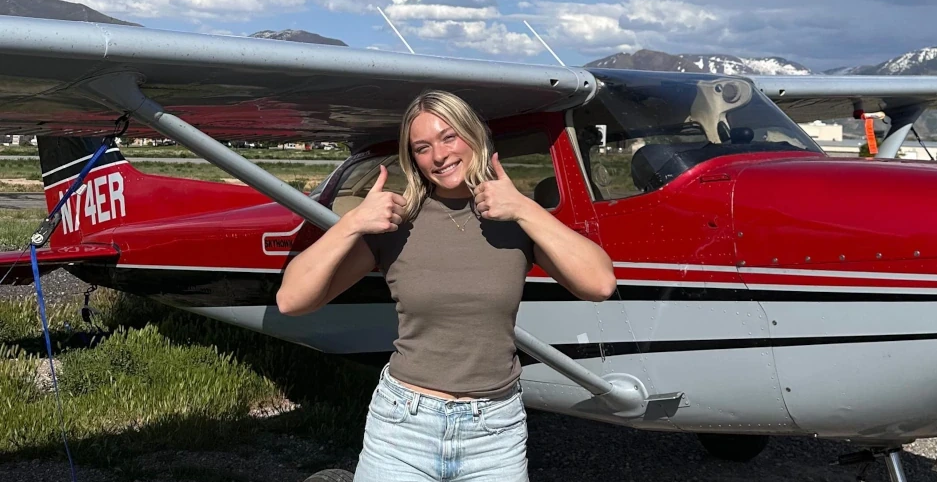 Woman smiling with both thumbs up in front of a Cessna 172