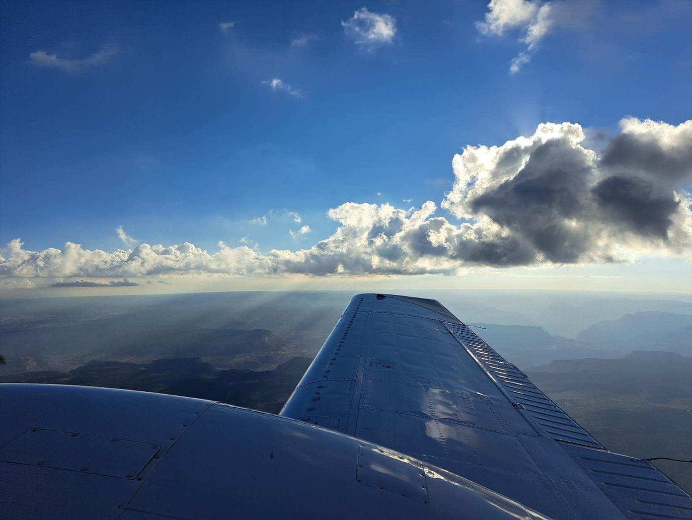 View over an airplane wing toward building cumulus clouds above Arizona desert terrain